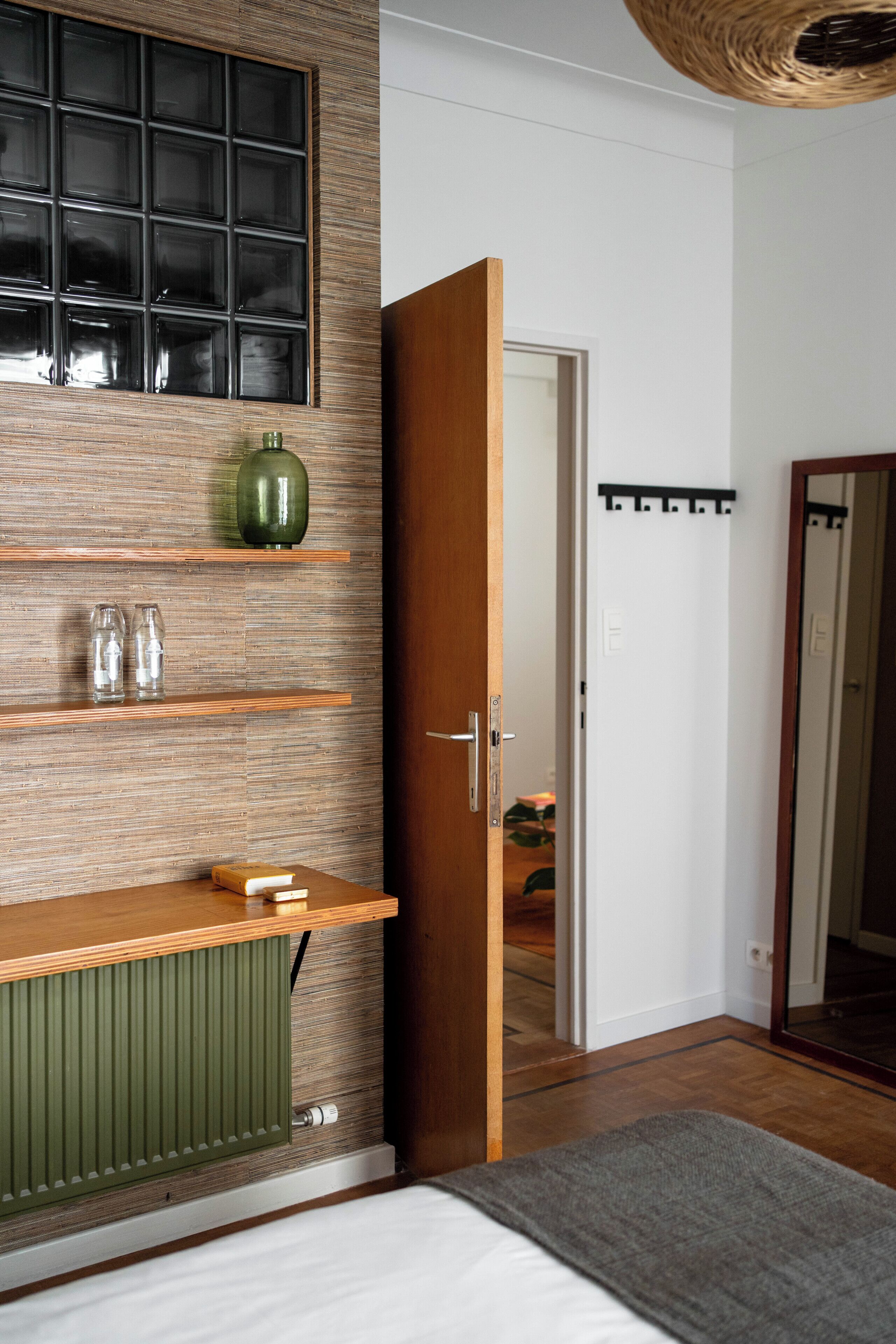 A bedroom with a wooden bed, a green radiator, a shelf with glass jars, and a door leading to another room.