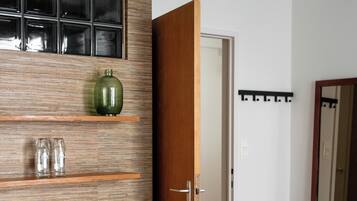 A bedroom with a wooden bed, a green radiator, a shelf with glass jars, and a door leading to another room.