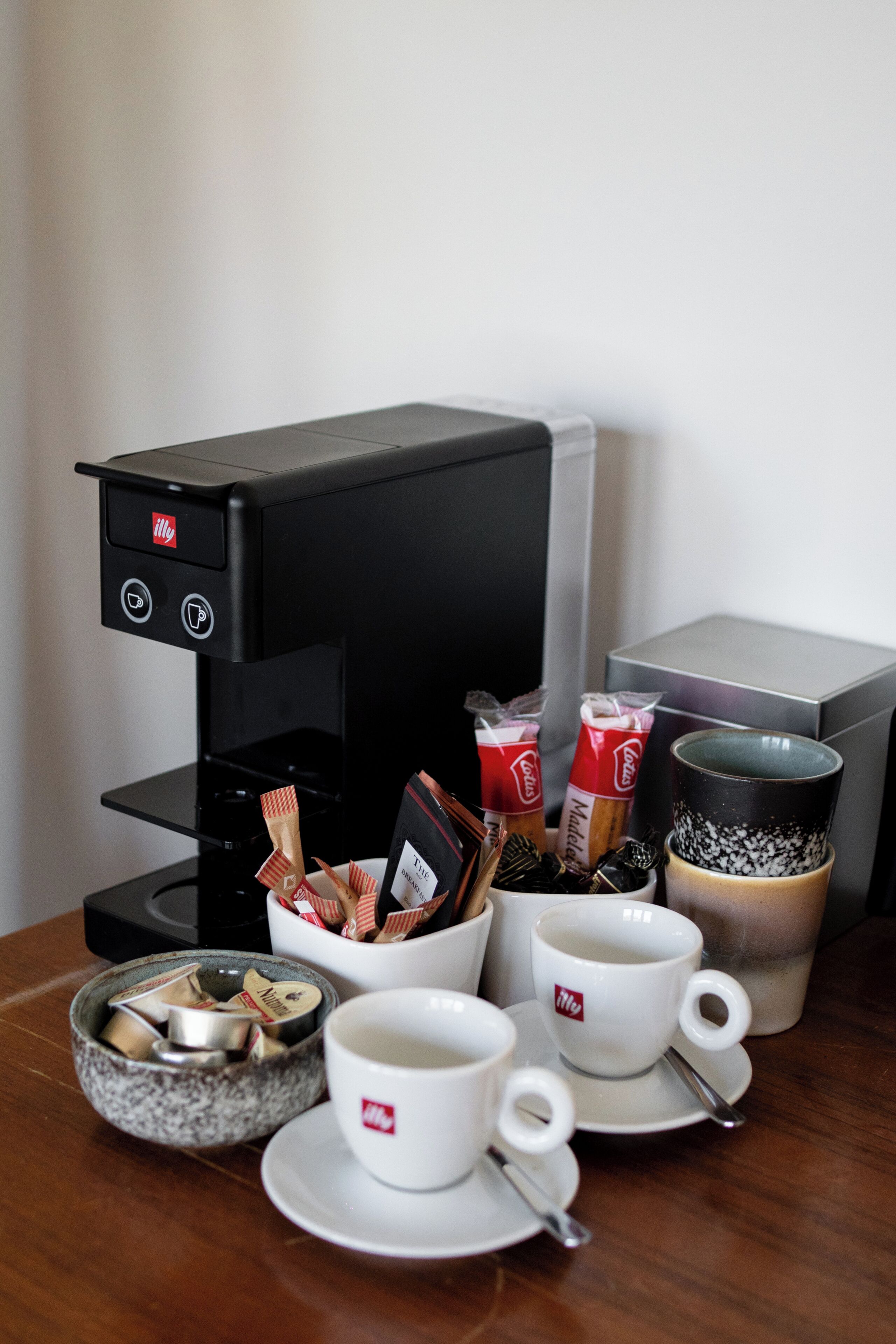 A coffee machine with a milk frother, a bowl of assorted chocolates, and a cup of coffee on a table.
