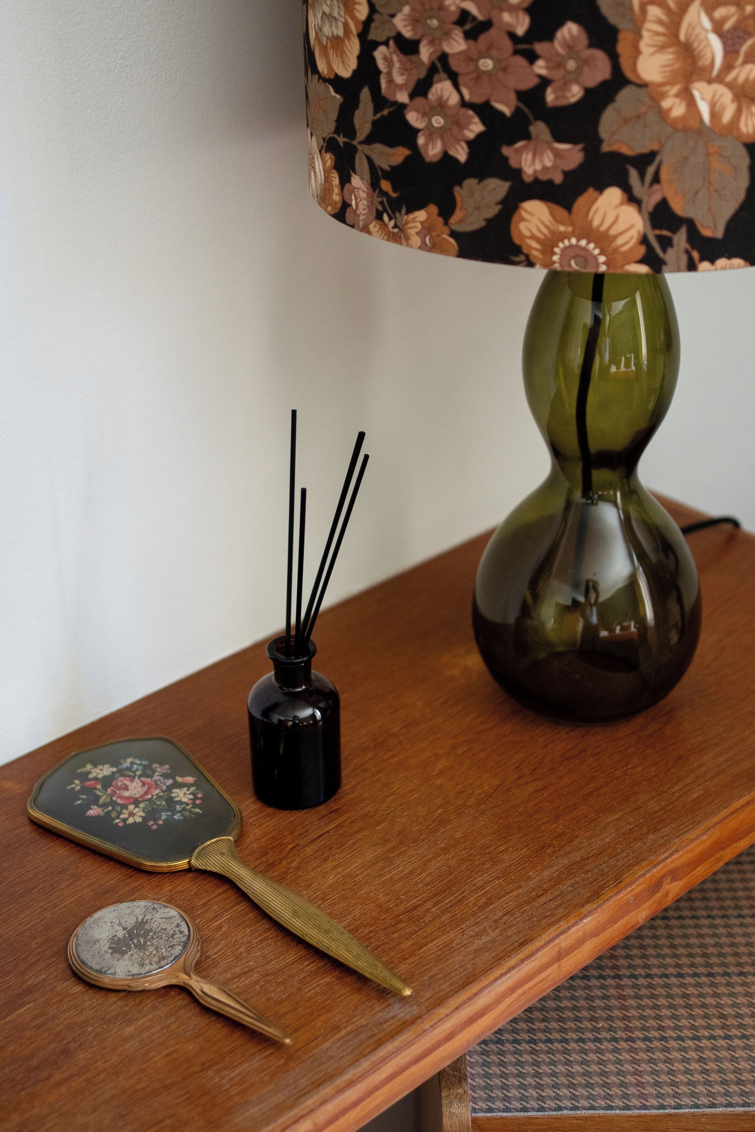 Una mesa de madera con un florero verde, un quemador de incienso negro, un abanico decorativo y un espejo redondo pequeño.