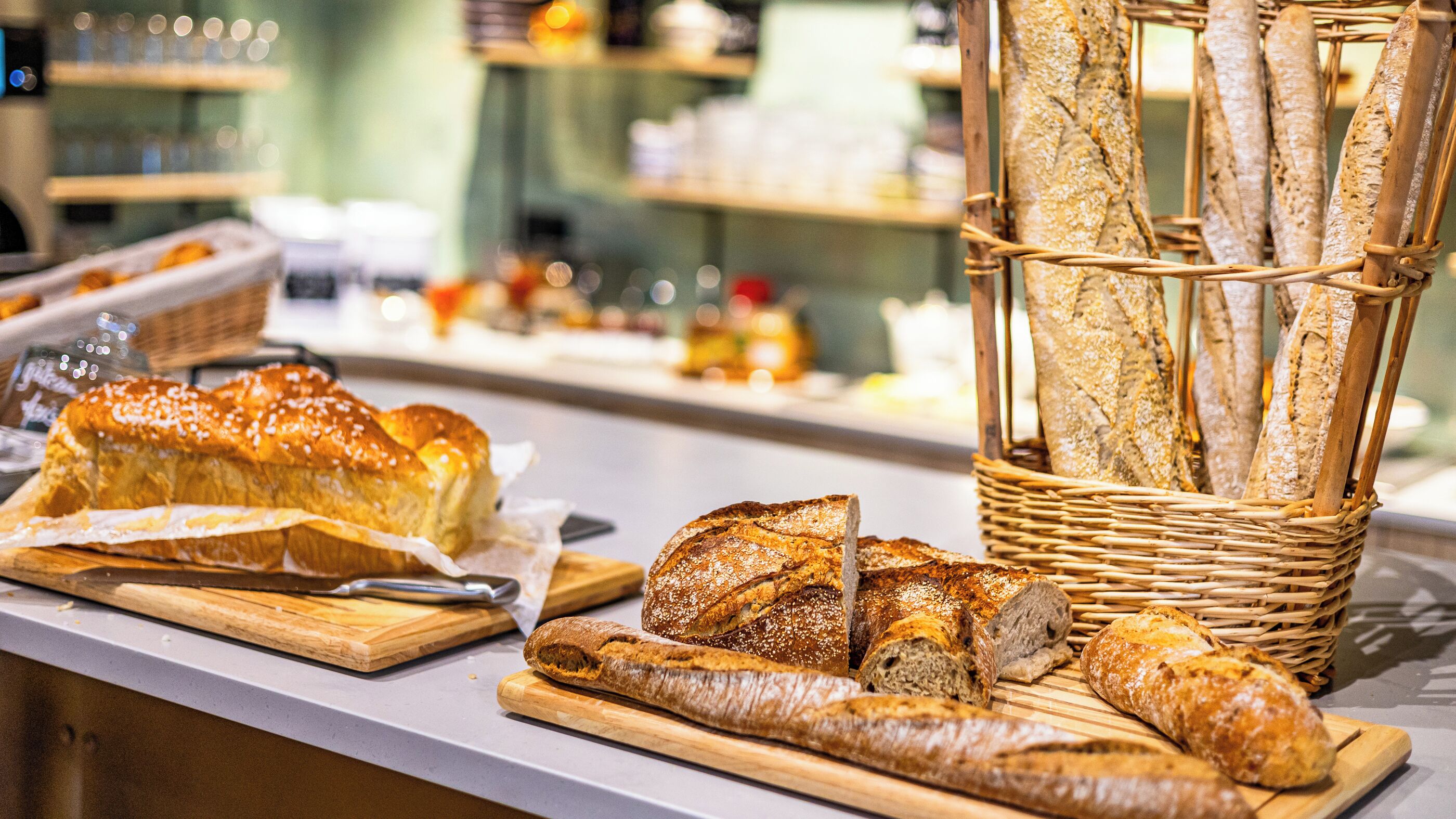 Verschiedene Brotsorten liegen auf einer Theke ausgestellt, darunter ein Brot mit Sesam und ein Korb mit Baguettes.