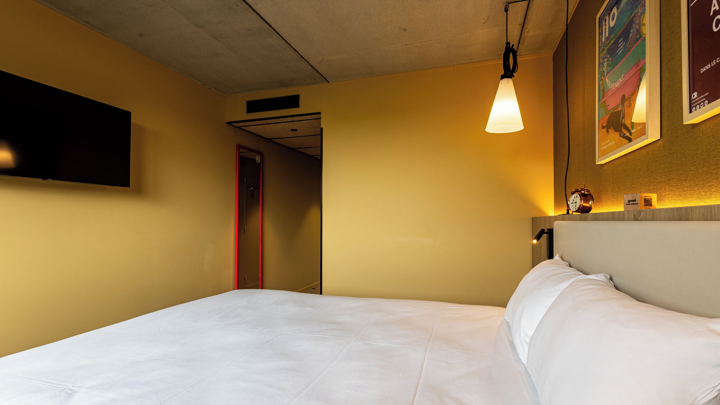A hotel room with a bed, a TV mounted on the wall, a clock, and a poster.