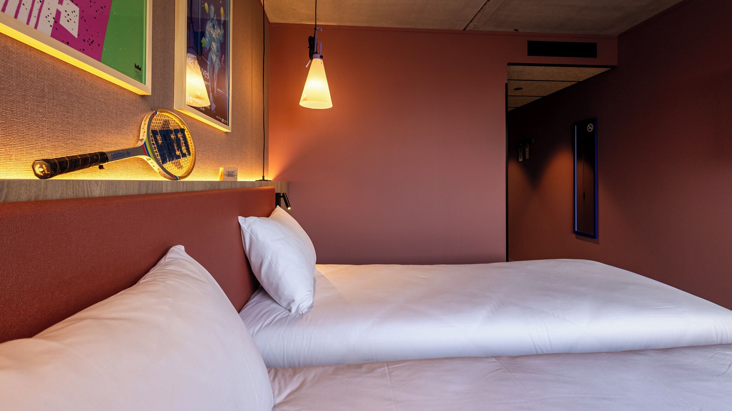 A hotel room with a bed, pillows, a wall-mounted lamp, and a framed picture.
