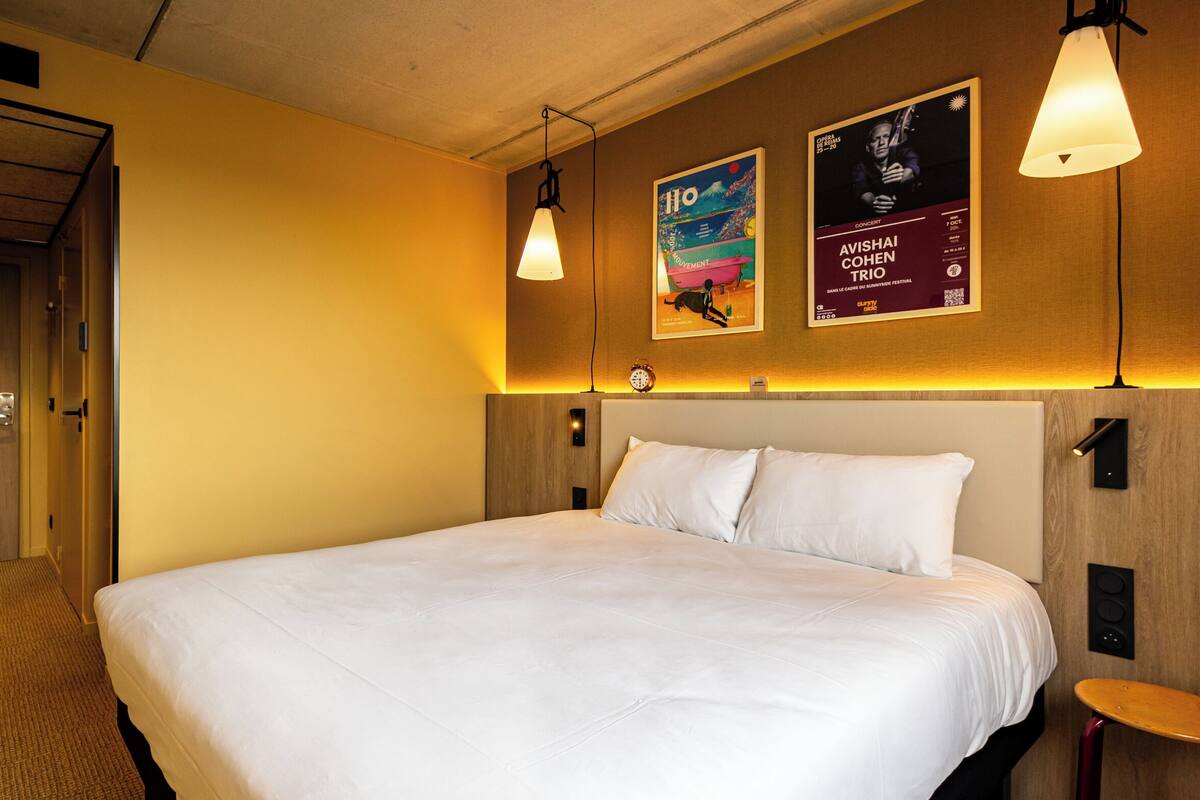 A hotel room with a large bed, wooden headboard, and two posters on the wall.
