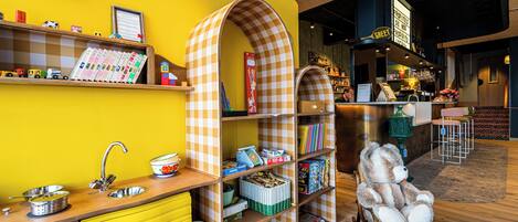 A brightly colored interior with a yellow wall, a checkered bookshelf, a sink, and a bar area.
