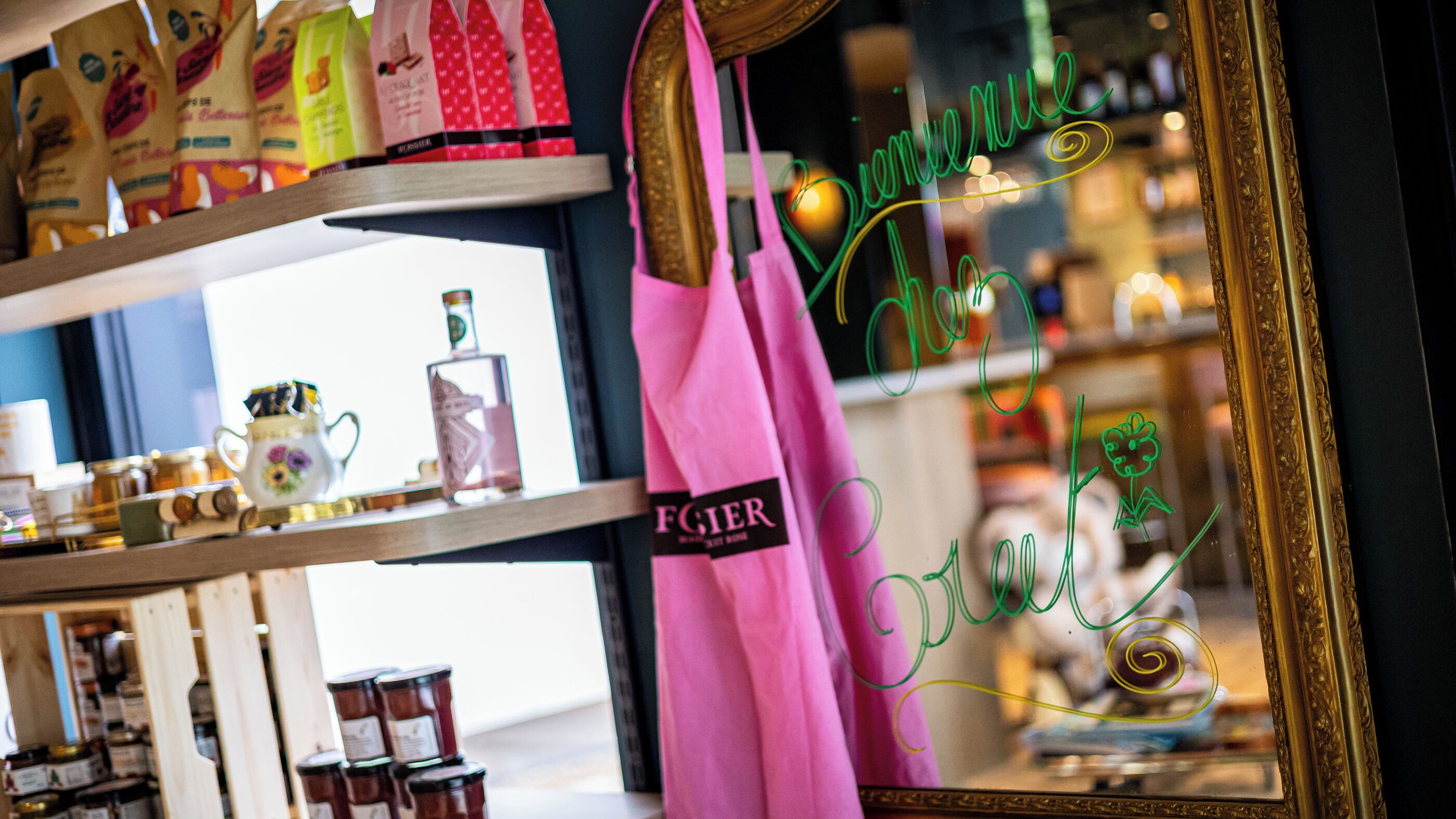 A store interior with shelves displaying various products, a pink bag hanging on a rack, and a mirror reflecting the interior.