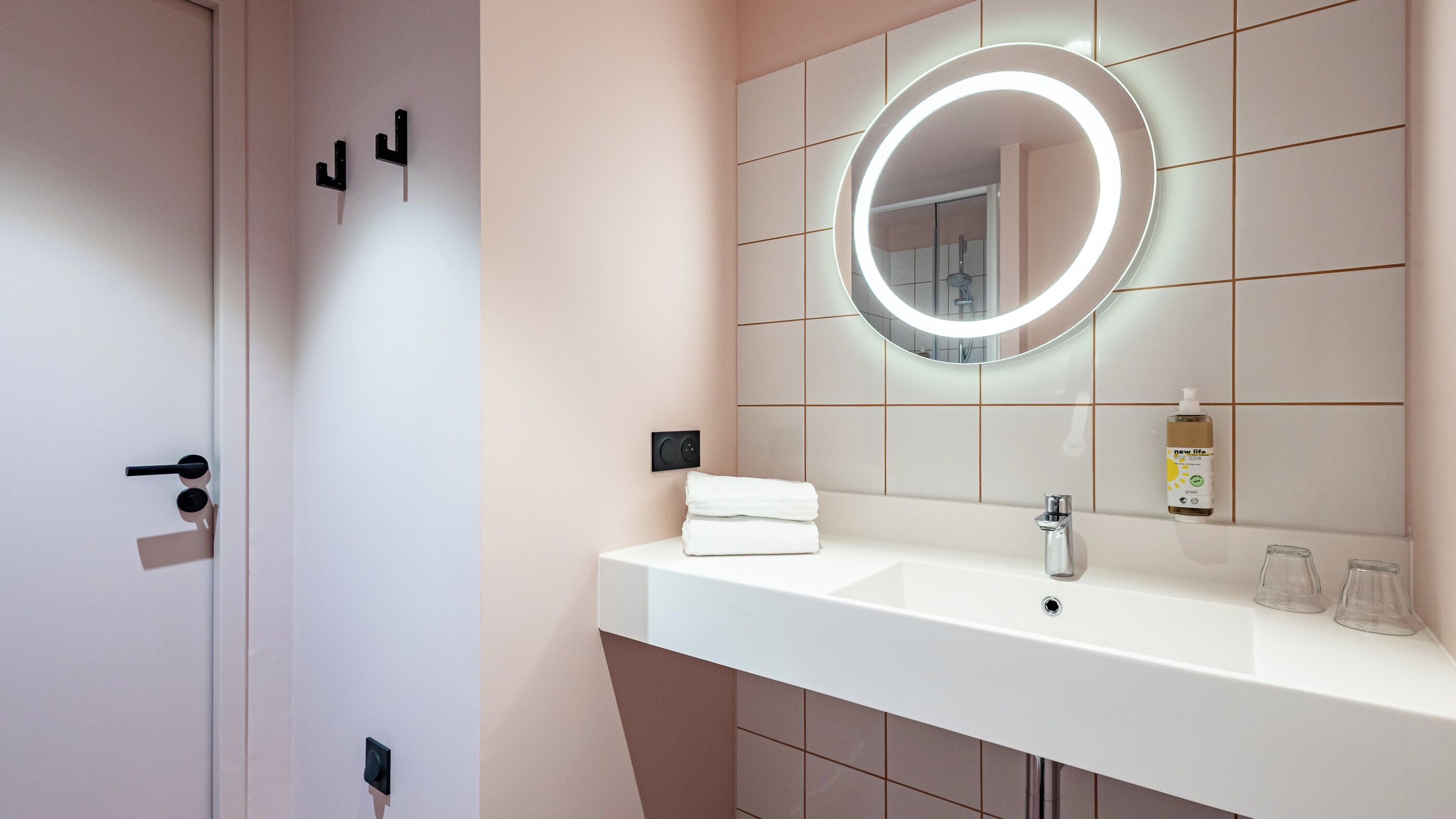A modern bathroom with a white sink, a round mirror with a light, and a towel on the counter.
