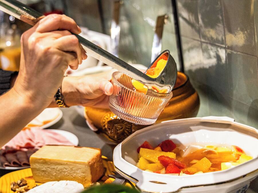 A person using tongs to serve fruit from a bowl.