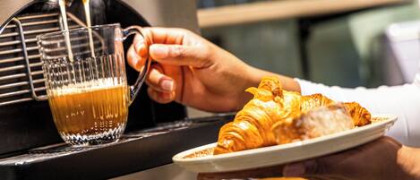 A hand holding a plate with a croissant and a glass of coffee.