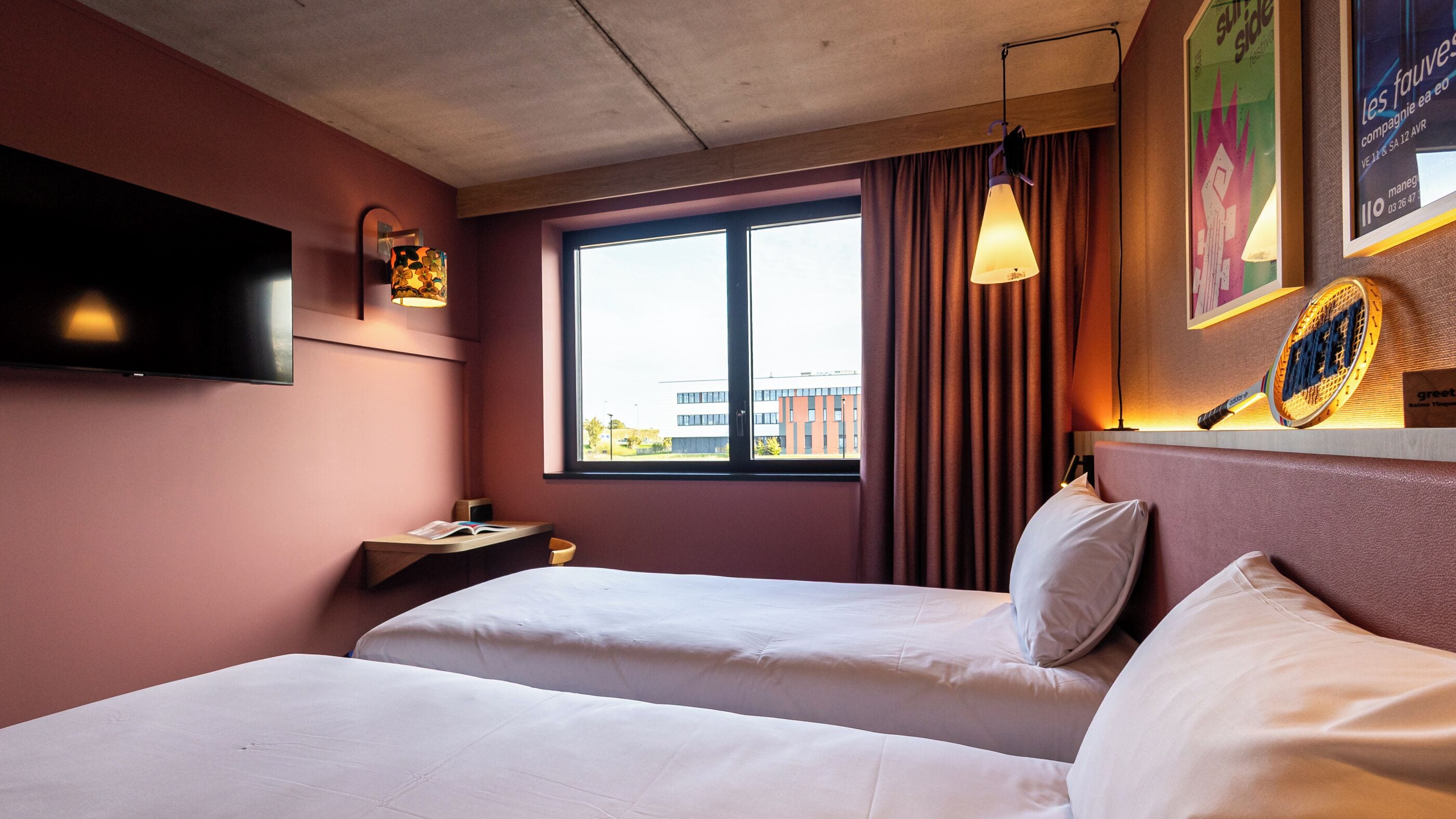 Ett hotellrum med två sängar, en tv som är monterad på väggen och ett fönster med gardiner.