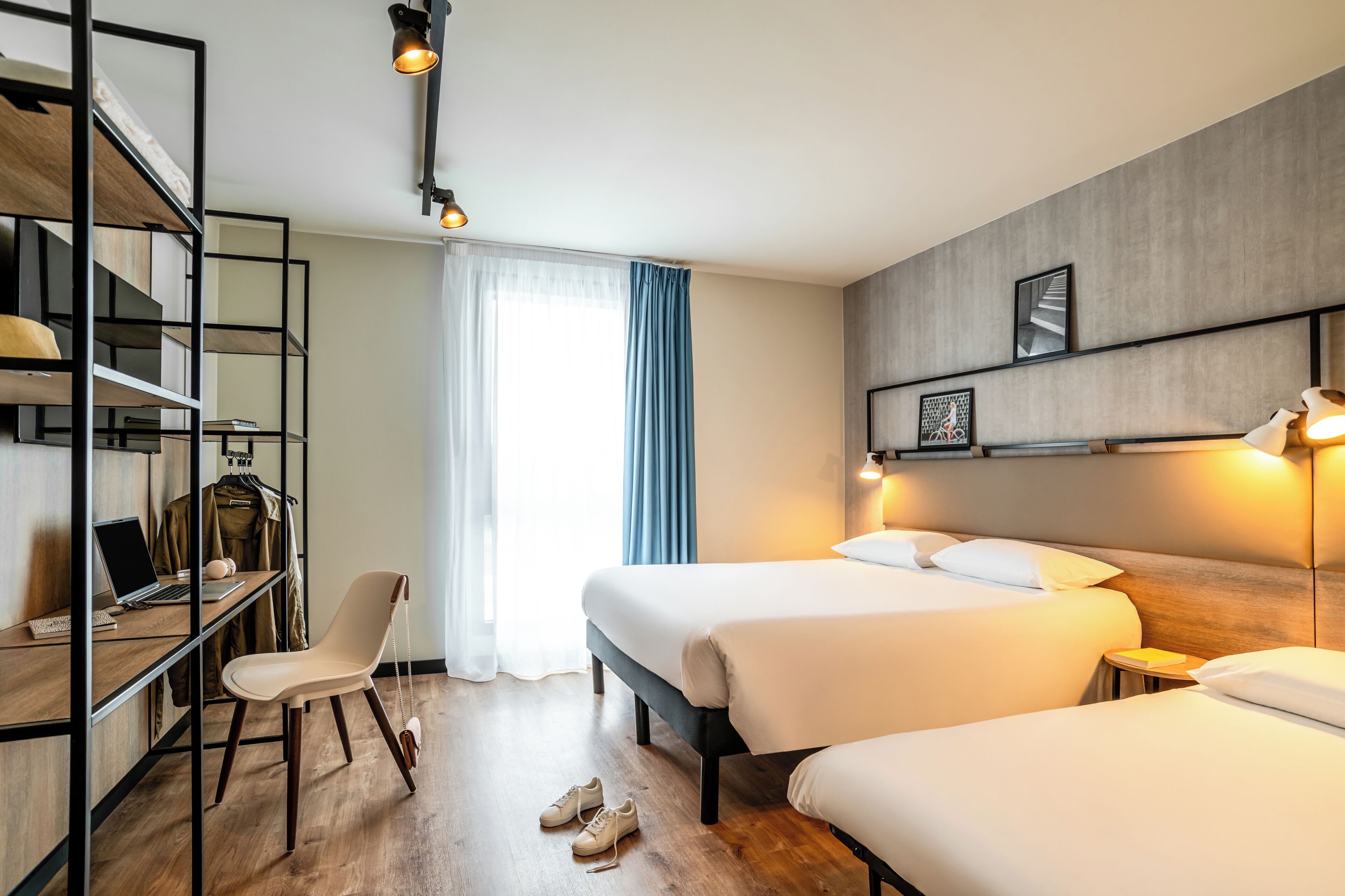 A hotel room with two beds, a desk with a laptop, a chair, and a wardrobe.
