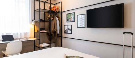 Een hotelkamer met een bed, een bureau met een laptop, een televisie, een kledingkast en een koffer.