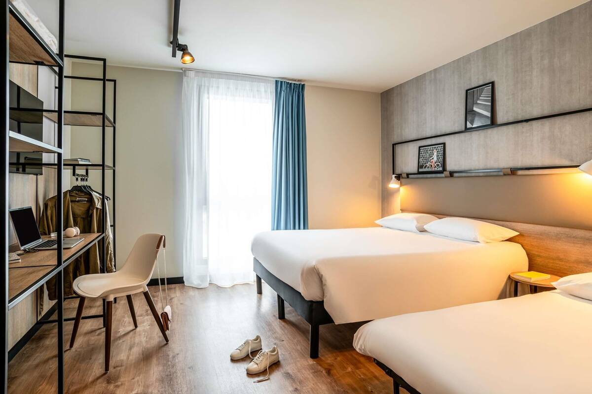 A hotel room with two beds, a desk with a laptop, a chair, and a wardrobe.