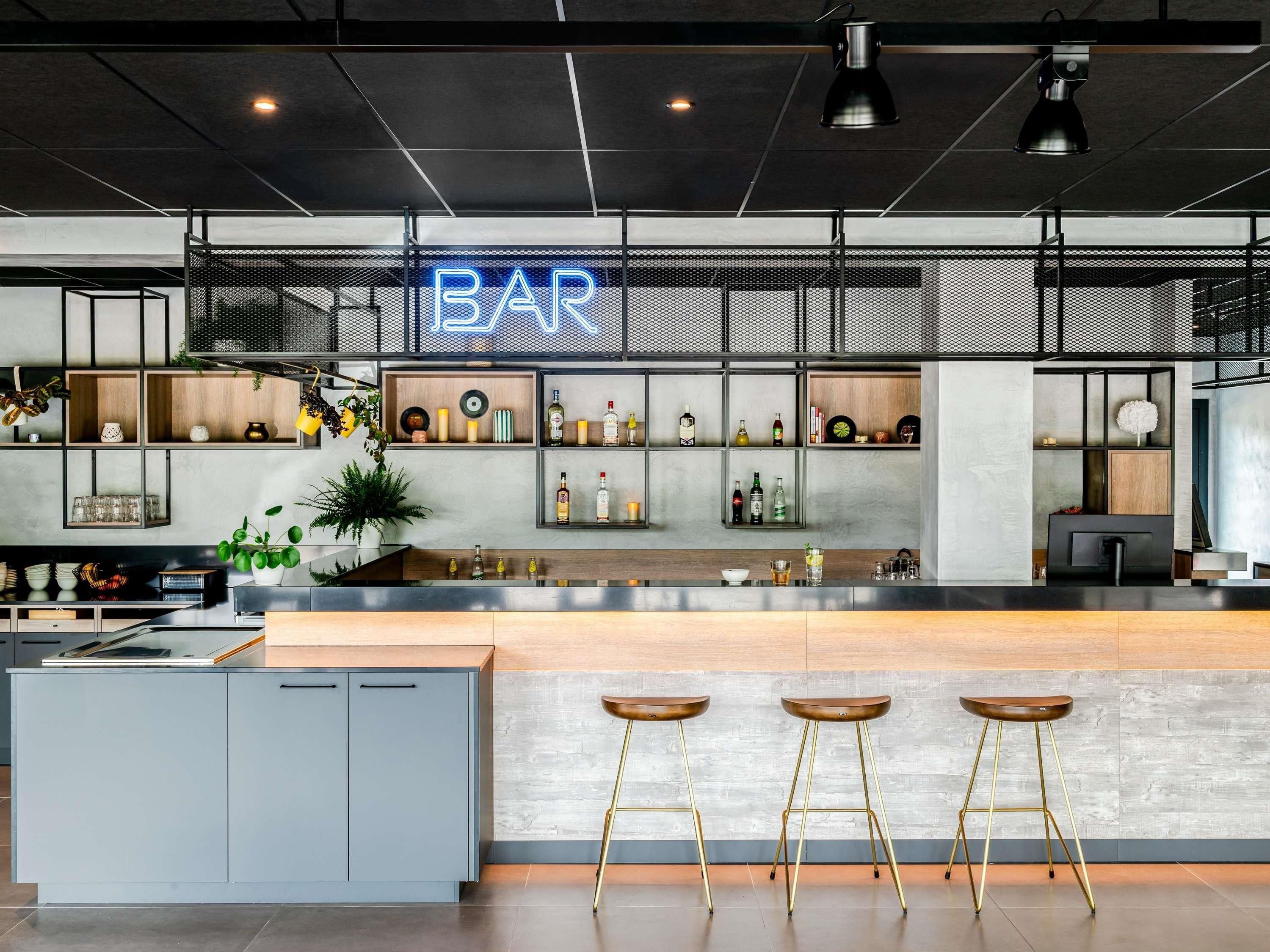 Un espace bar moderne avec un panneau néon, des étagères remplies de bouteilles et des tabourets.