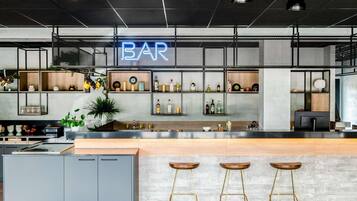 Un espace bar moderne avec un panneau néon, des étagères remplies de bouteilles et des tabourets.