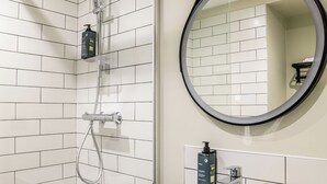 Un baño moderno con ducha envuelta en vidrio, lavamanos blanco con espejo y artículos de aseo en la encimera.