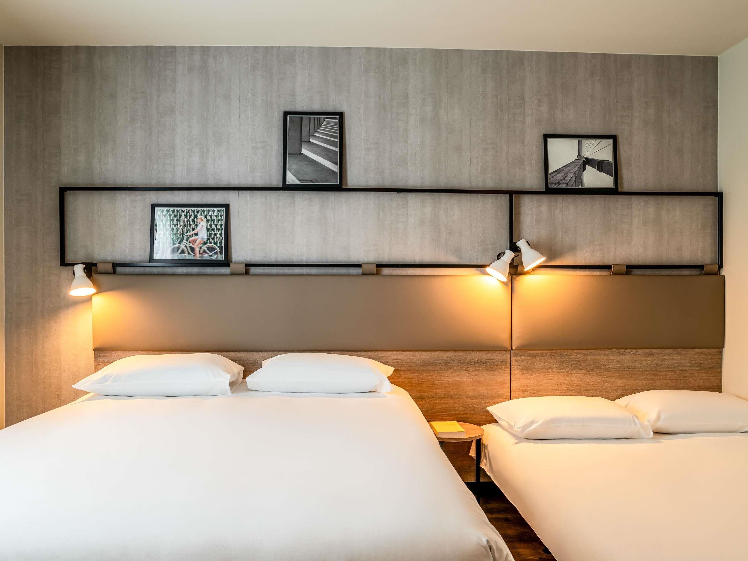 A hotel room with two beds, a headboard with built-in lighting, and framed pictures on the wall.