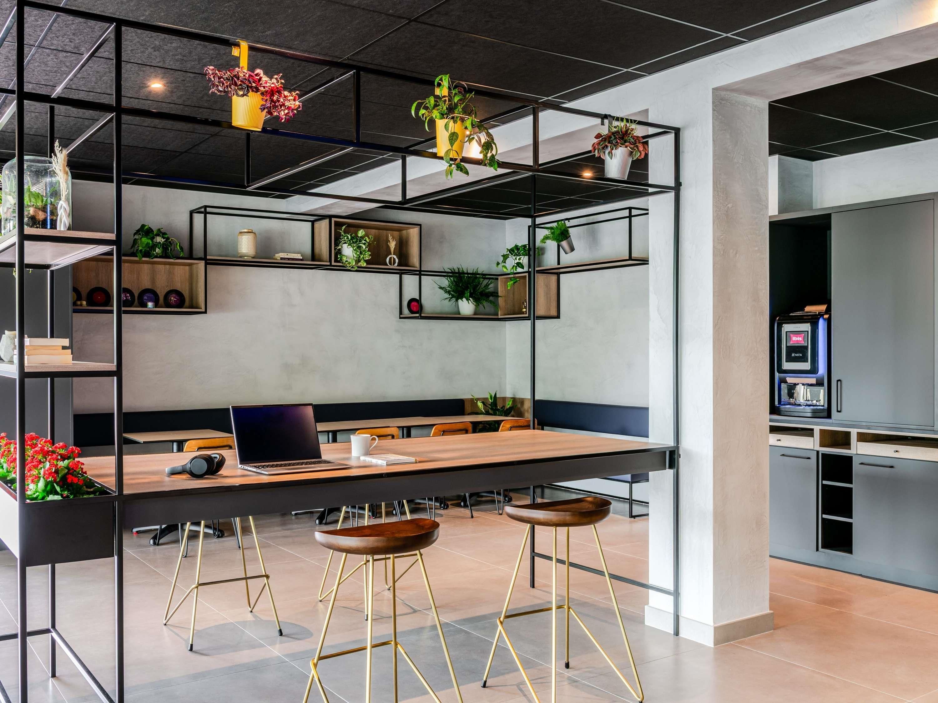 Un ambiente ufficio moderno con un lungo tavolo, diverse sedie, un laptop e una macchina per caffè.