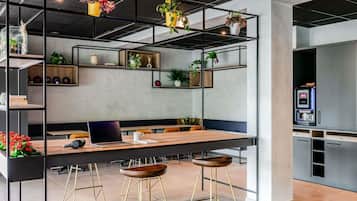 Un ambiente ufficio moderno con un lungo tavolo, diverse sedie, un laptop e una macchina per caffè.