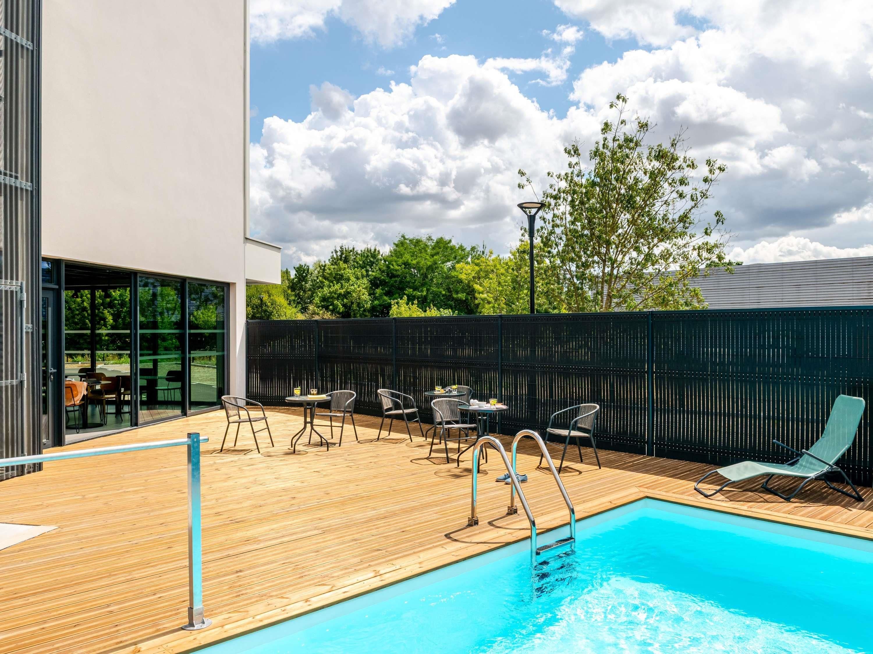 A swimming pool with a wooden deck, outdoor seating, and a view of the sky.