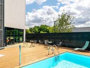 Una piscina con bordo in legno, area relax all'aperto e vista sul cielo.