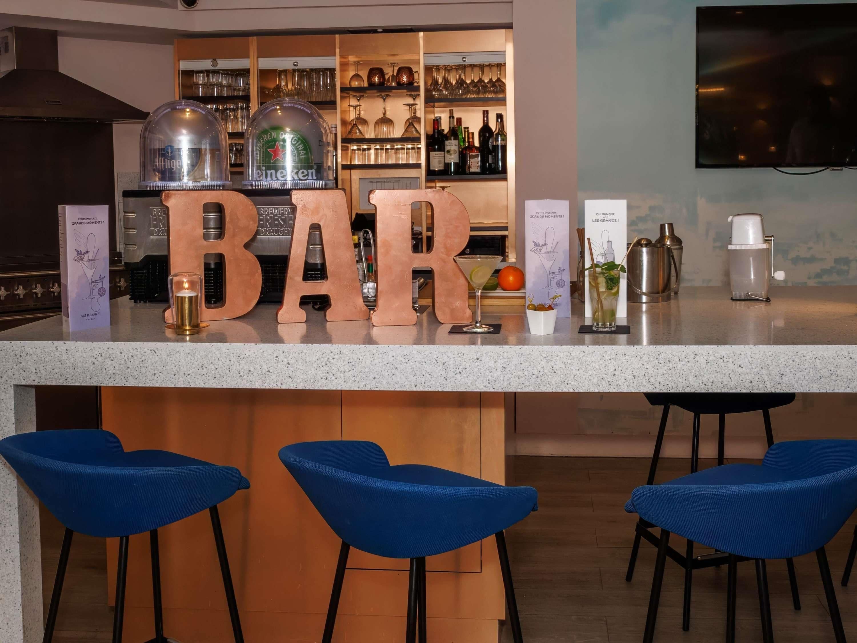 Zona de bar con mostrador, taburetes y un fondo de botellas y copas de vino.