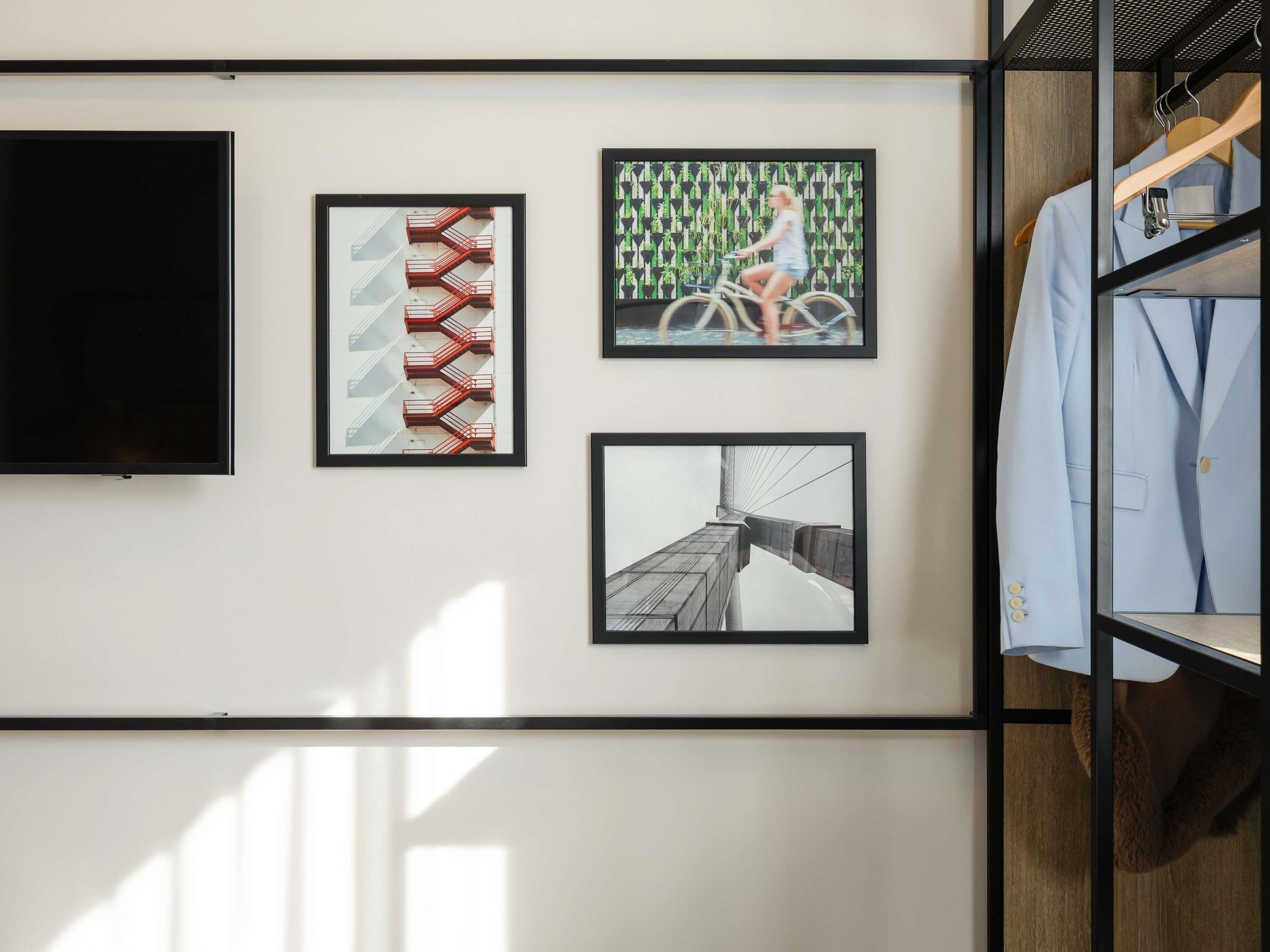 Una pared con tres cuadros enmarcados, un televisor y un perchero.