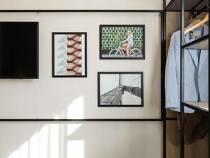 A wall with three framed pictures, a television, and a clothing rack. - ibis Bordeaux Nord Carbon Blanc (Carbon-Blanc)