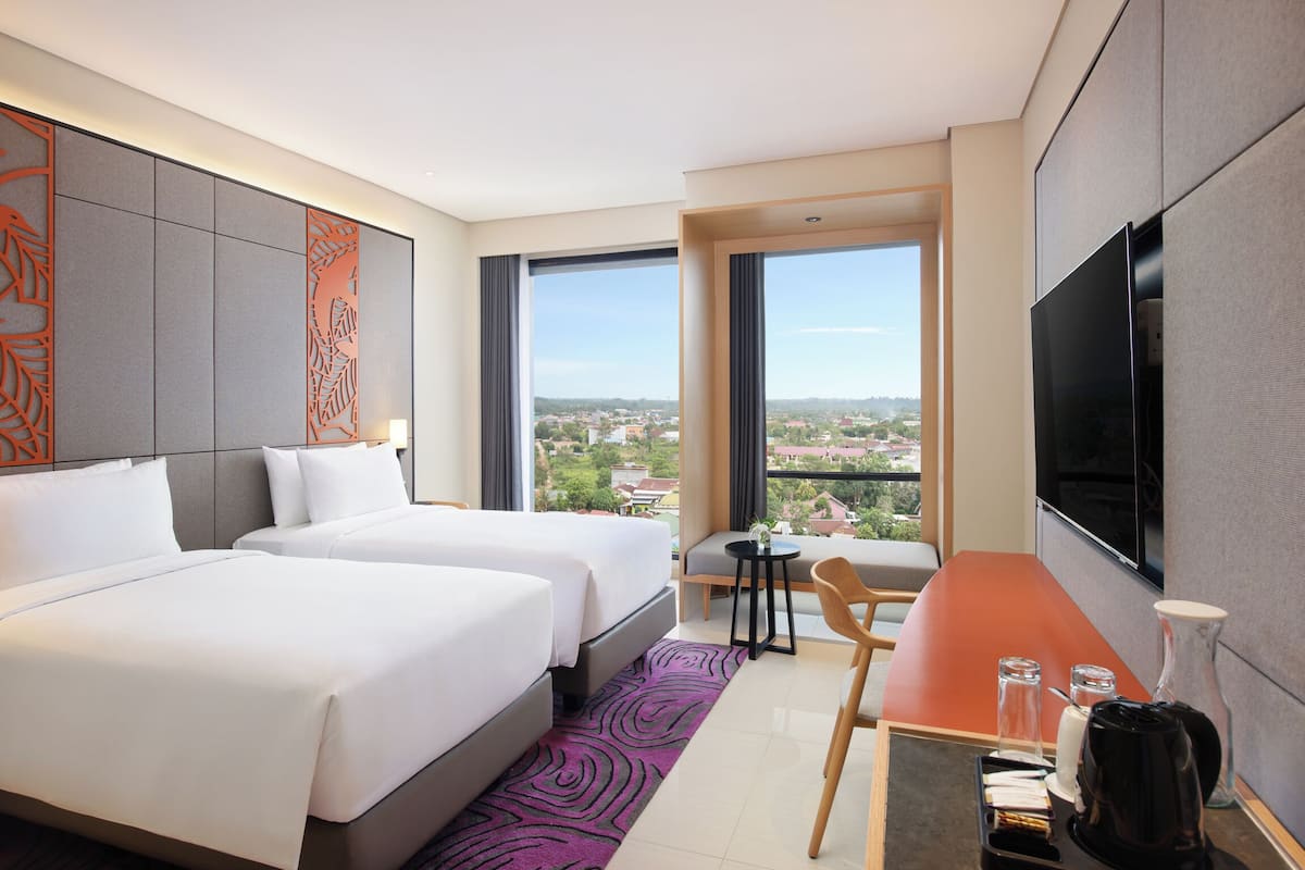 A hotel room with two beds, a dining table, a TV, and a view of the city.