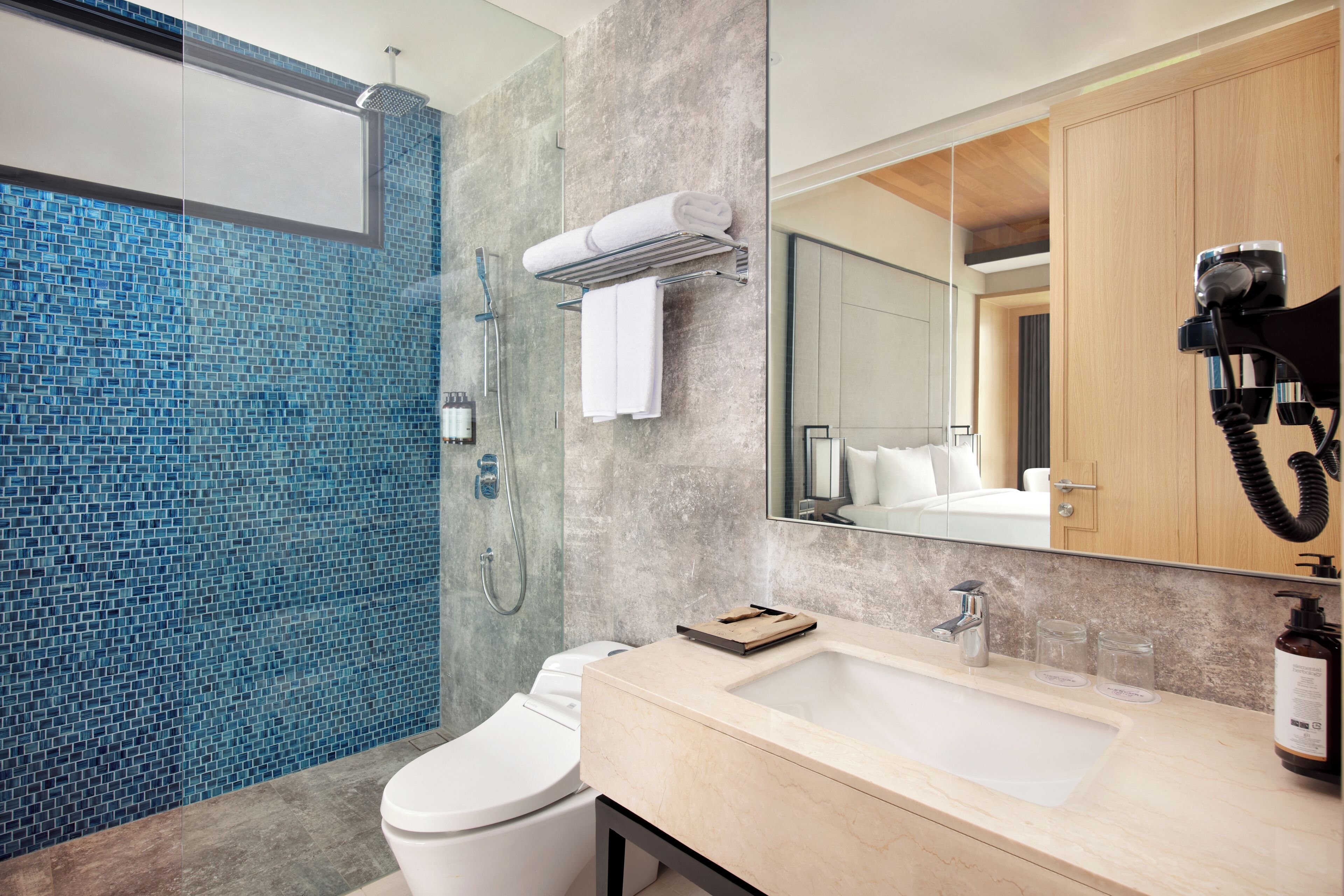 Un baño moderno con cabina de ducha de vidrio, inodoro blanco, lavabo color beige con espejo y un mueble de madera.