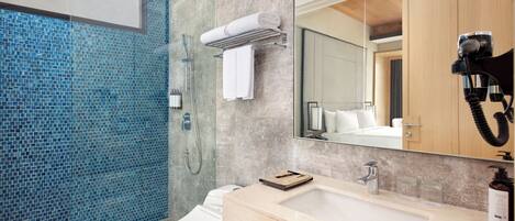 Un baño moderno con cabina de ducha de vidrio, inodoro blanco, lavabo color beige con espejo y un mueble de madera.