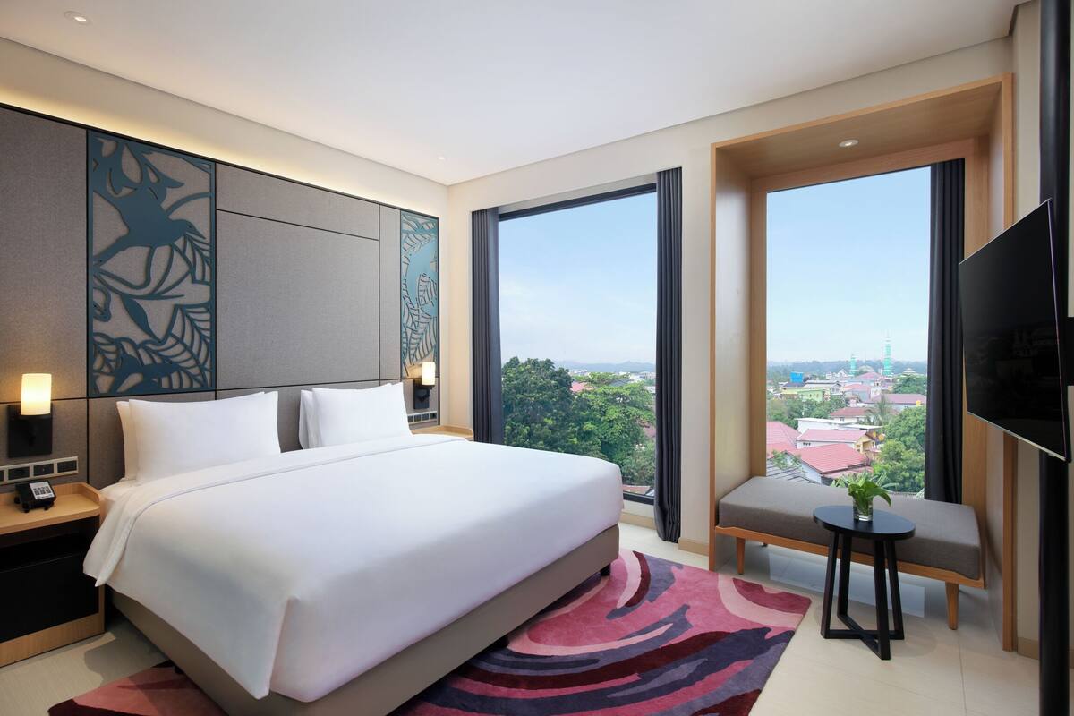 A modern hotel room with a large bed, a seating area, a television, and a city view.