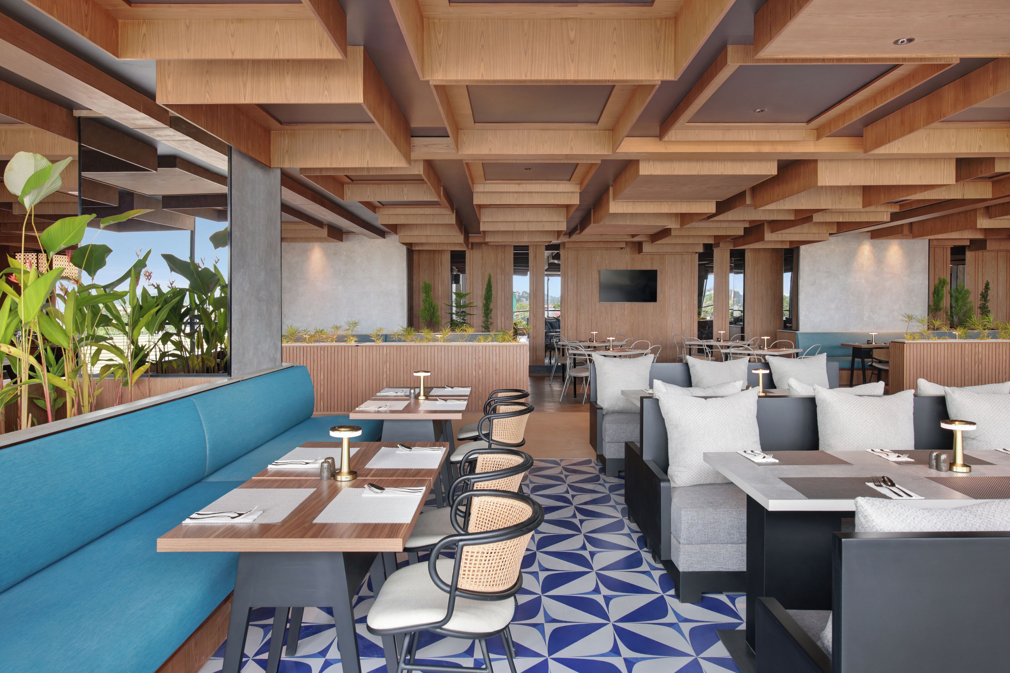 En moderne restaurant med træbjælker i loftet, gulv med blå og hvide mønstre, og forskellige siddepladser inklusive båse og borde.