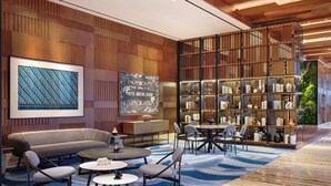 A modern hotel lobby with a wooden panel wall, a large abstract painting, a seating area with sofas and tables, and a bookshelf filled with decorative items. - Mercure Berau (Tanjung Redeb)