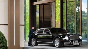 A black luxury car parked in front of a building with large windows and a green patterned wall.