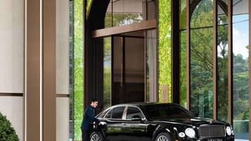 Un automóvil de lujo negro estacionado frente a un edificio con grandes ventanales y un muro verde con estampado.
