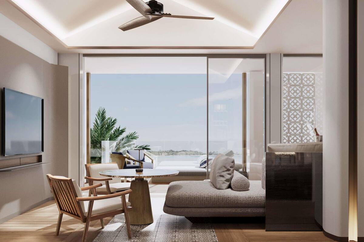 A modern living room with a ceiling fan, a TV mounted on the wall, a round table with chairs, a sofa, and a view of the ocean through large glass doors.