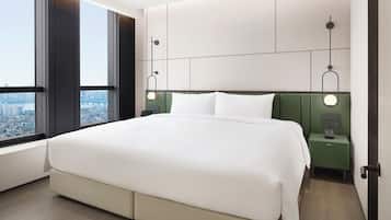 Habitación de hotel moderna con una cama grande, vista a la ciudad, cabecera verde y mesitas de noche con lámparas.
