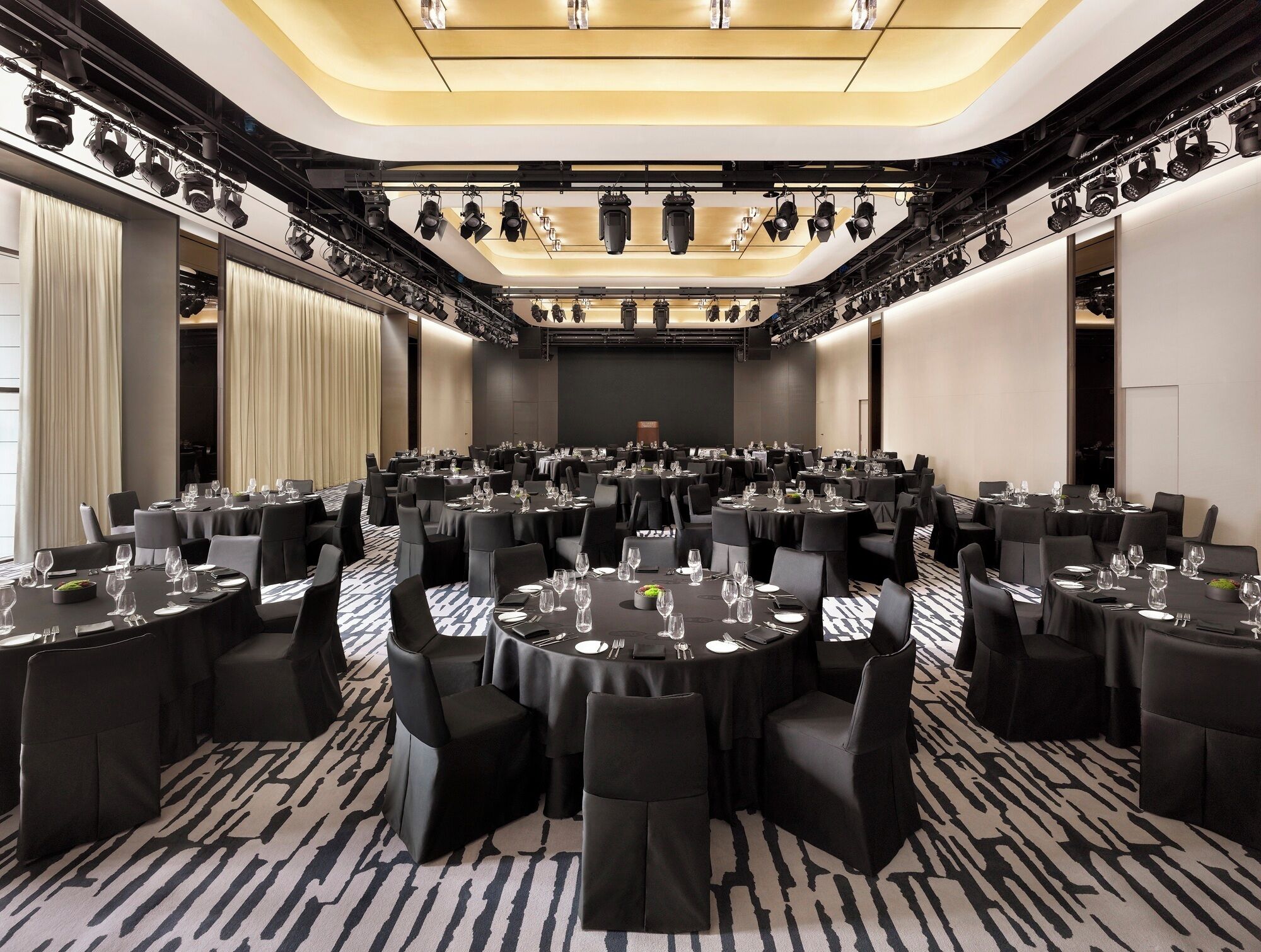 Un salón de conferencias con mesas redondas, sillas negras y un escenario con iluminación.