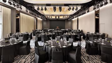 Un salón de conferencias con mesas redondas, sillas negras y un escenario con iluminación.