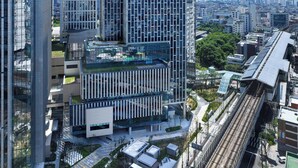 Un edificio moderno de gran altura con fachada de diseño geométrico y amplios ventanales, rodeado de otros edificios contemporáneos y un cielo despejado.