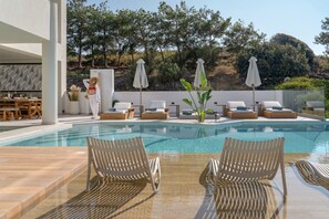 Uma área de piscina com espreguiçadeiras, um bar e uma pessoa perto da piscina.
