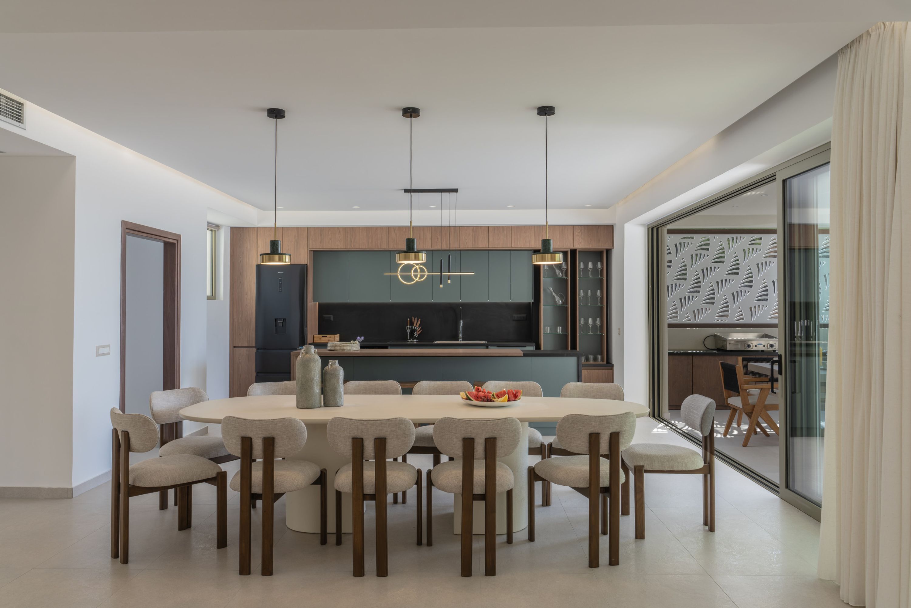 Un comedor moderno con una mesa redonda, varias sillas, iluminación colgante y una cocina al fondo.