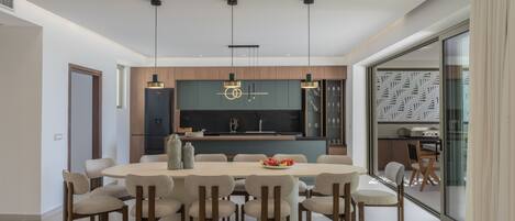 Un comedor moderno con una mesa redonda, varias sillas, iluminación colgante y una cocina al fondo.
