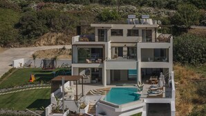 A modern multi-story house with a large swimming pool, outdoor seating, and a well-maintained garden. - Luxurious Villa Selestine - With Private Pool (Mylopotamos)