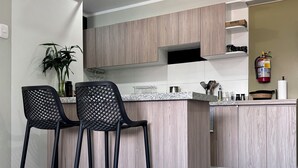 A modern kitchen with two black bar stools, a countertop with kitchen utensils, and a fire extinguisher mounted on the wall.
