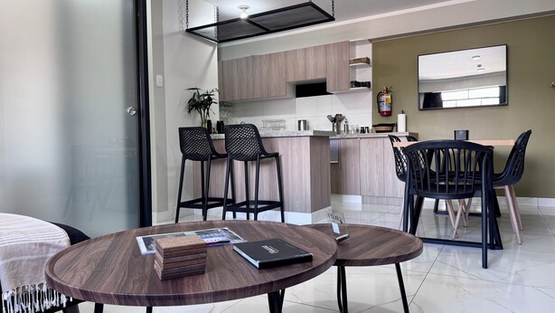 A modern kitchen with wooden cabinets, a built-in stove, and a dining area with two round tables and chairs.