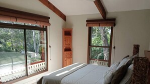 Ein Schlafzimmer mit einem Bett, einem Holzschrank und großen Fenstern mit Blick ins Grüne.
