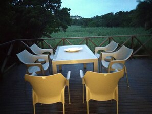 Une table et des chaises sur une terrasse extérieure, avec vue sur un champ verdoyant et des arbres.