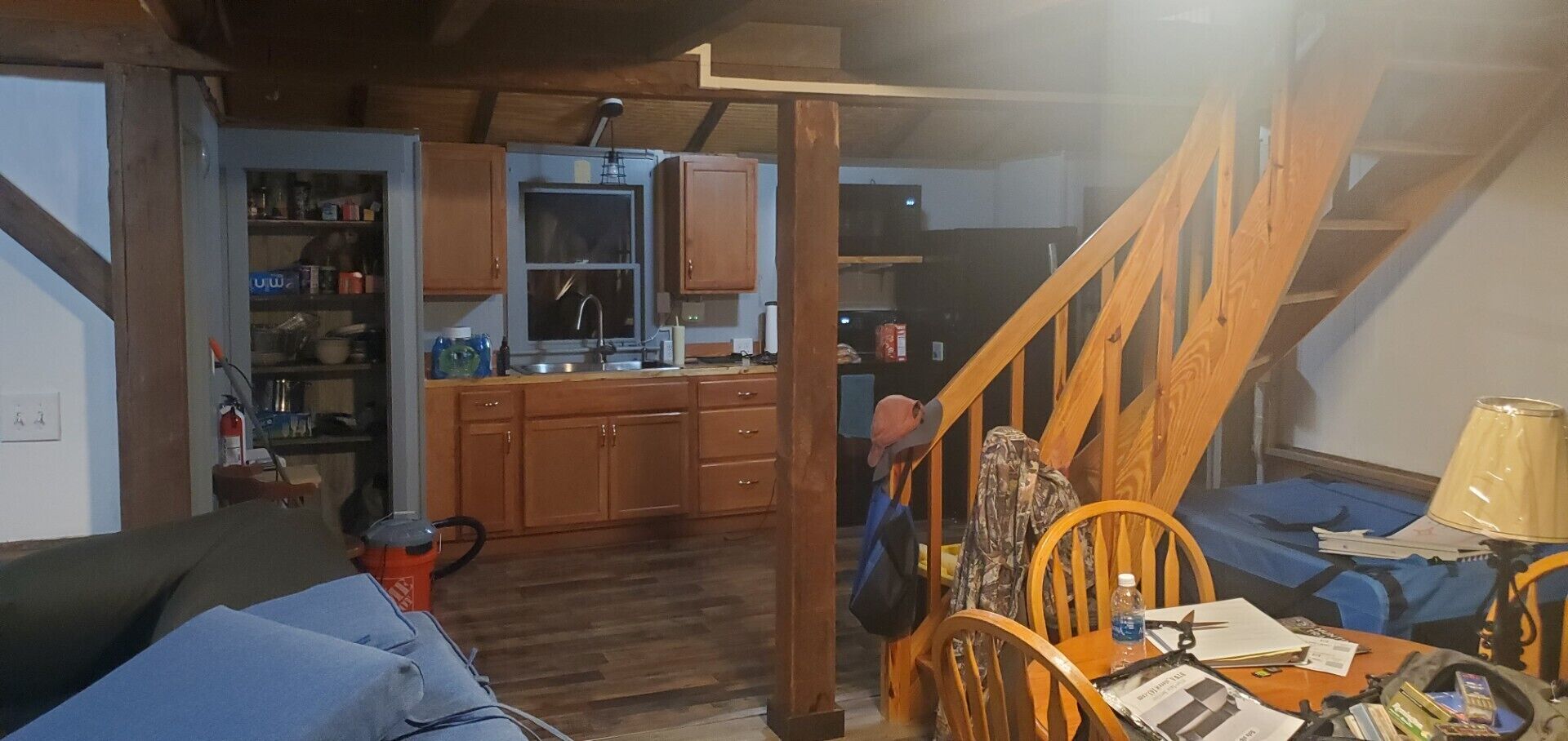 A cozy living room with a wooden staircase, a kitchen area with wooden cabinets, and a dining table with chairs.